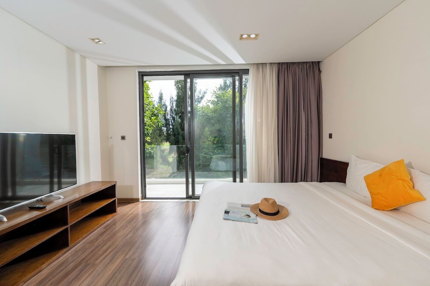 A modern hotel room with a large bed, a flat-screen TV, and a sliding glass door leading to a balcony.