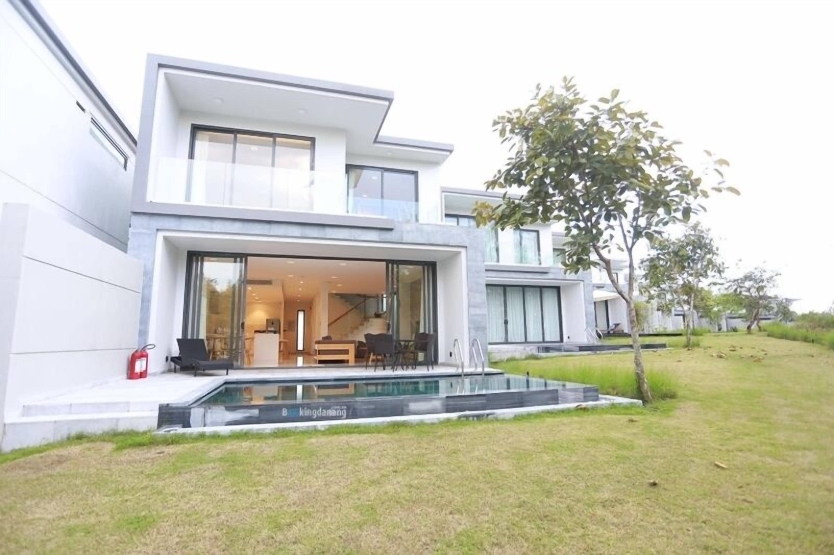 A modern two-story house with a large glass door entrance, a swimming pool, and a well-maintained lawn.