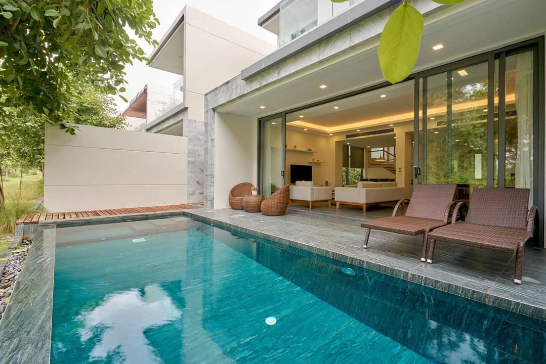 Een modern huis met een zwembad, een terras en een glazen deur die leidt naar een woonkamer.