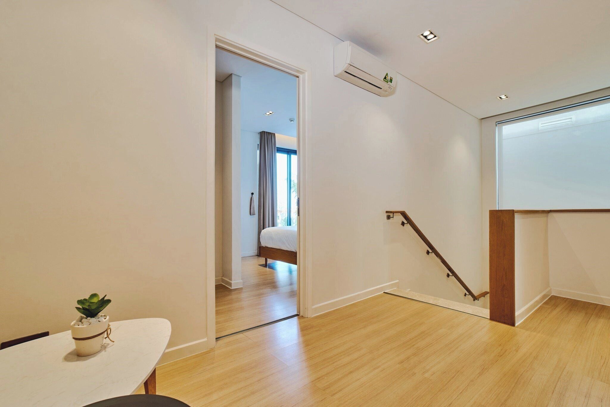 Habitación de hotel moderna con suelo de madera, pared blanca, una pequeña planta en maceta y una escalera que lleva a otra habitación.