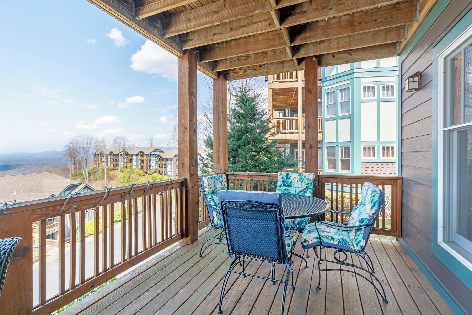 Eine Holzterrasse mit Tisch und Stühlen, mit Blick auf eine Berglandschaft und ein Gebäude mit blauen Verzierungen.