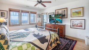 Une chambre à coucher comprenant un lit, un téléviseur, un ventilateur de plafond et une vue sur l’extérieur grâce à de grandes fenêtres.