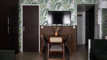 Een eetgedeelte met een aan de muur bevestigde televisie, een houten eettafel met stoelen en een deur links.