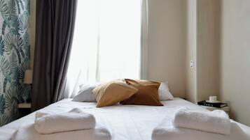 Ein Hotelzimmer mit Bett, Kissen, einem Nachttisch mit Tasse und Buch sowie einem Fenster mit Vorhängen.