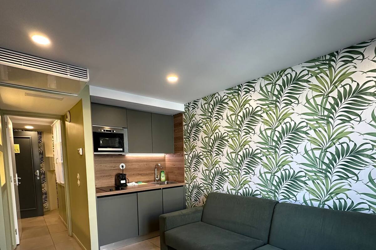 Eine moderne Küche mit integriertem Mikrowellenherd, Spüle und Kaffeemaschine. Im Wohnbereich befindet sich ein grünes Sofa und eine Wand mit Muster.