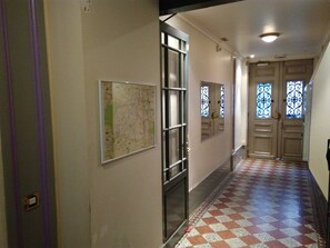 Un couloir avec une carte accrochée au mur, une porte dotée d’un miroir et un sol à motifs.