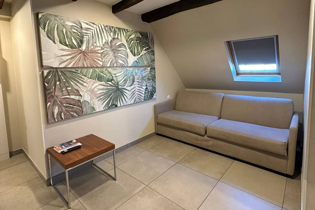 Ein gemütliches Wohnzimmer mit einem großen Kunstwerk mit einem tropischen Blatt, einem beigen Sofa, einem kleinen Holztisch und einem Oberlicht.