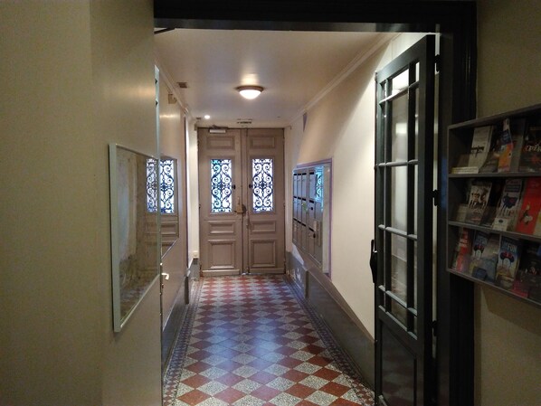 Un couloir doté d’un revêtement de sol à motifs, de portes à double battant avec des panneaux de verre décoratifs et d’une bibliothèque remplie de livres.