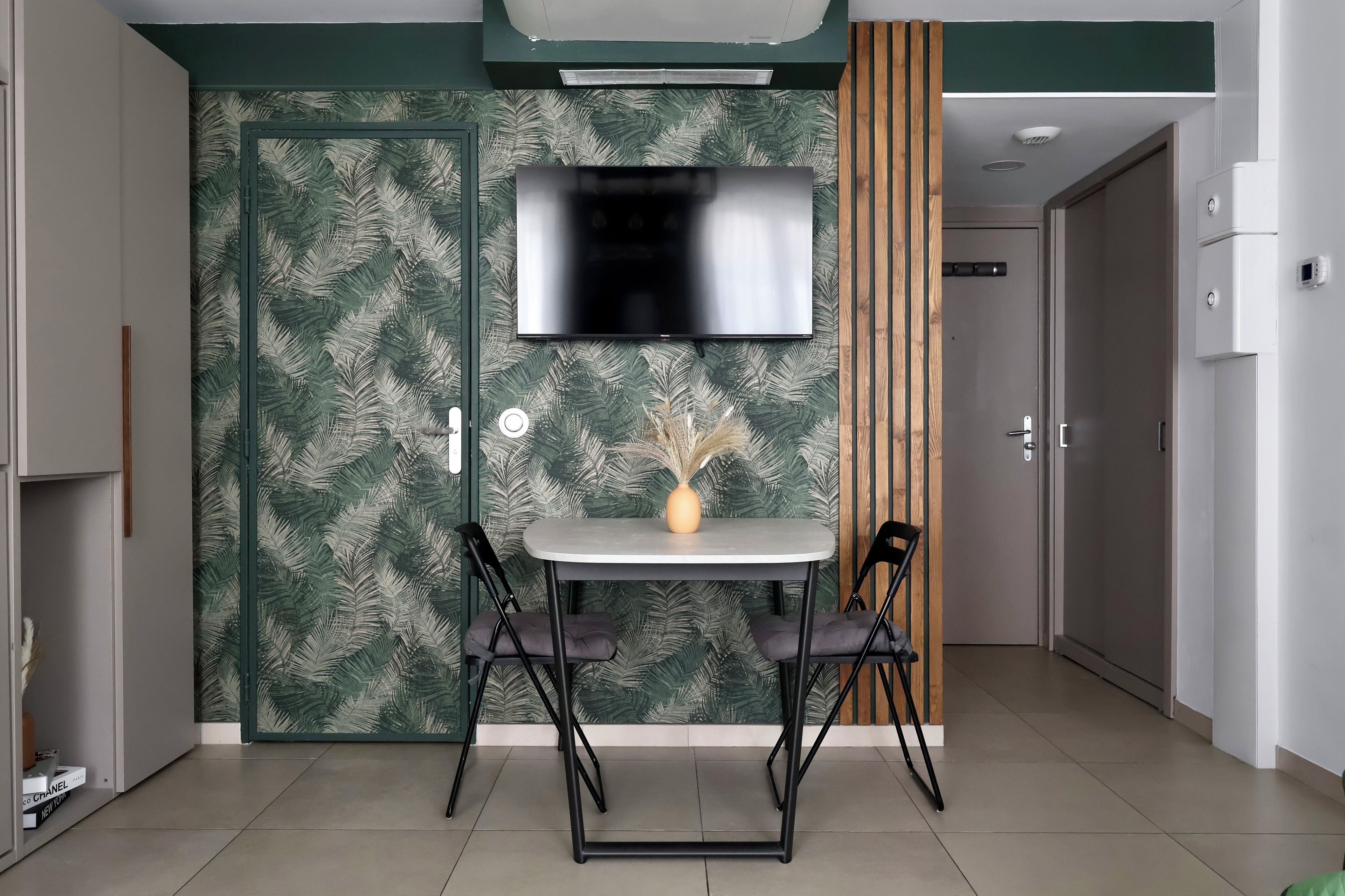 Ein modernes Zimmer mit einem flachbildfernseher an der Wand, einem kleinen Tisch mit Stühlen und einer Tür im Hintergrund.