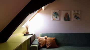 Een kamer met een groene bank, een klein tafeltje met een boek getiteld 'NEW YORK', en drie kunstwerken aan de muur.