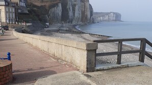Un paseo marítimo con sendero pavimentado, una construcción de ladrillo y barandilla de madera con vistas al mar.