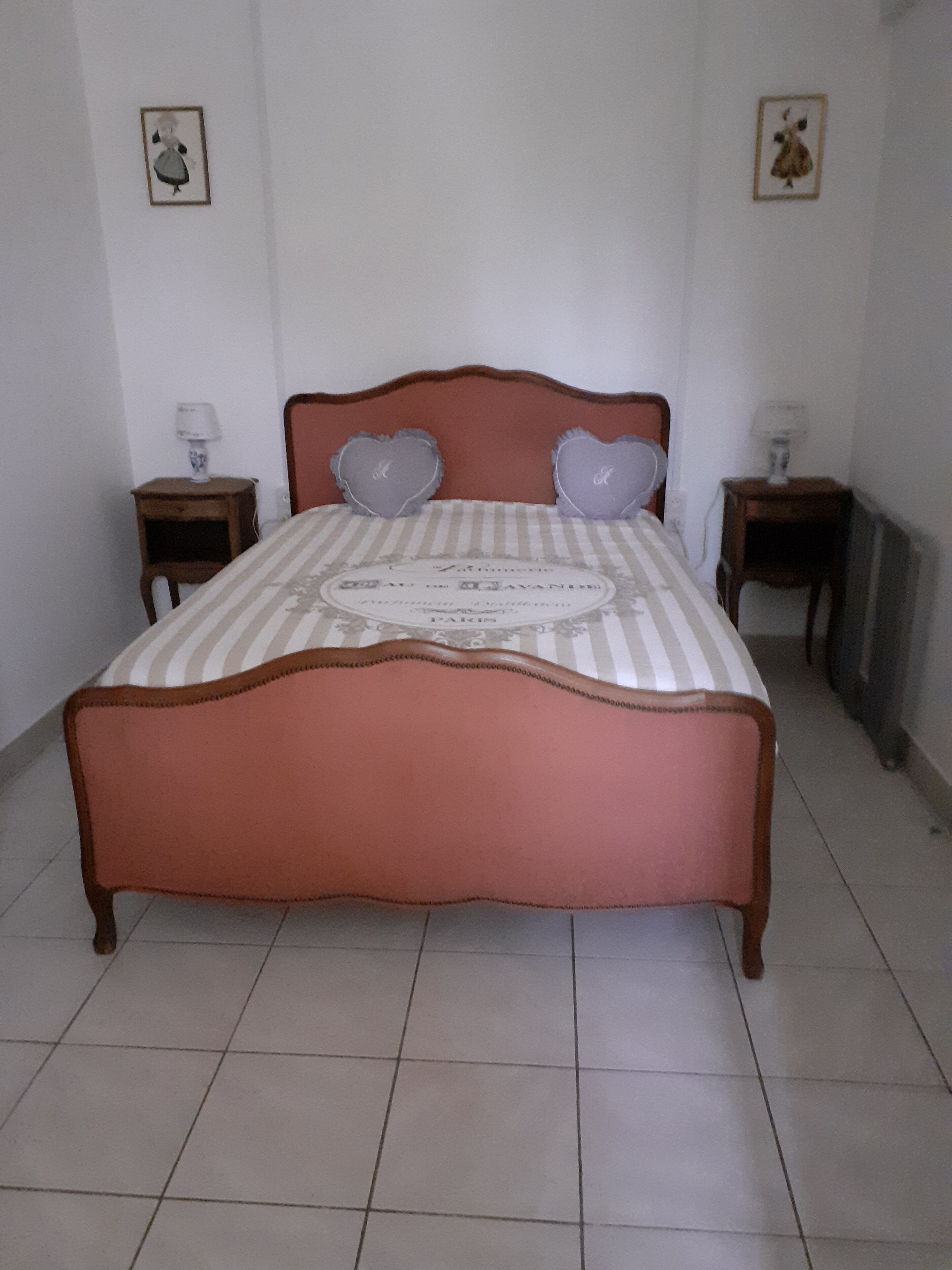 A bed with a striped bedspread and heart-shaped pillows, two bedside tables with lamps, and a framed picture on the wall.