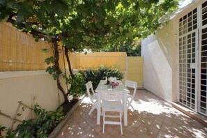 A patio with a table and chairs, surrounded by a yellow fence and a tree providing shade.