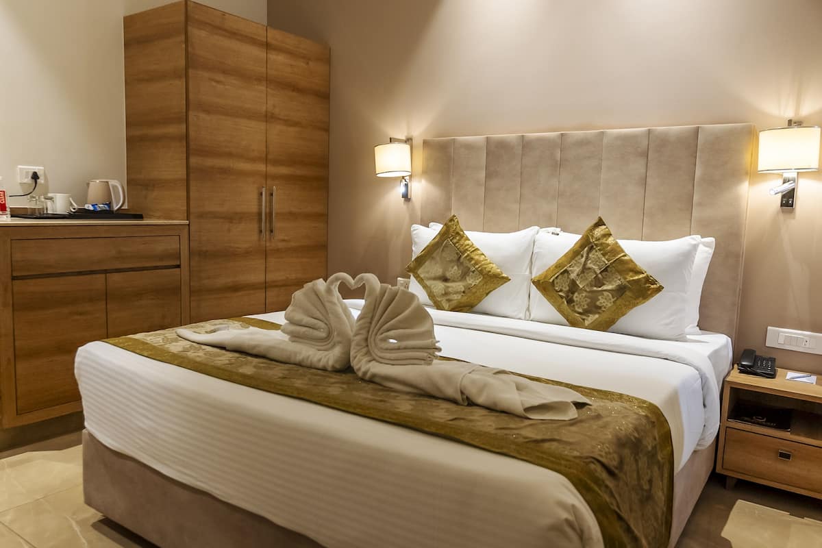 Una habitación de hotel con una cama, un armario de madera, una mesita de noche y una lámpara de pared.