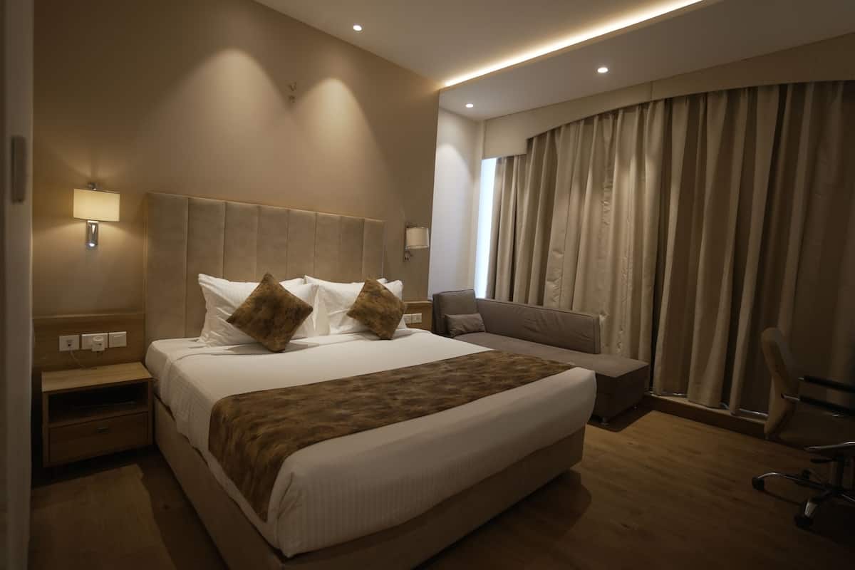 Una habitación de hotel con una cama grande, una mesita de noche, una lámpara, una silla y una ventana con cortinas.