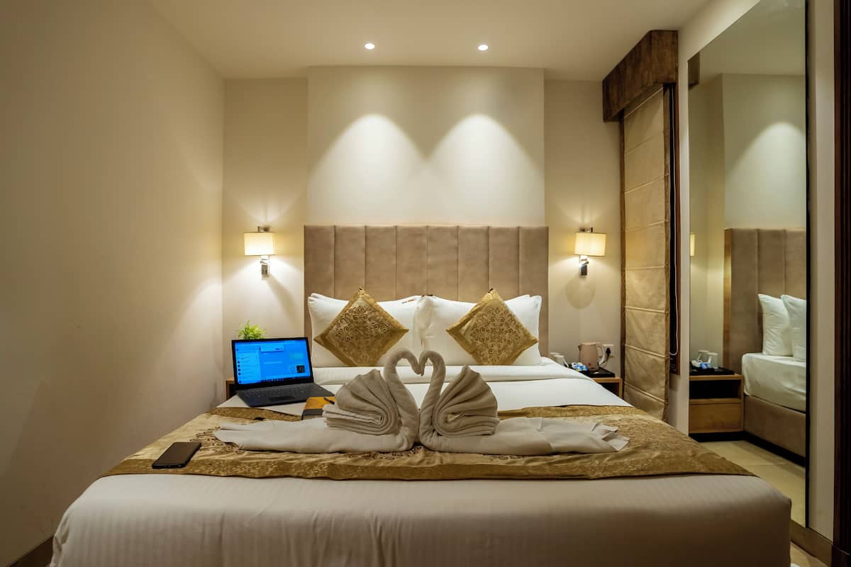 Habitación de hotel con una cama bien hecha, un ordenador portátil sobre la mesita de noche y un teléfono inteligente en la cama.