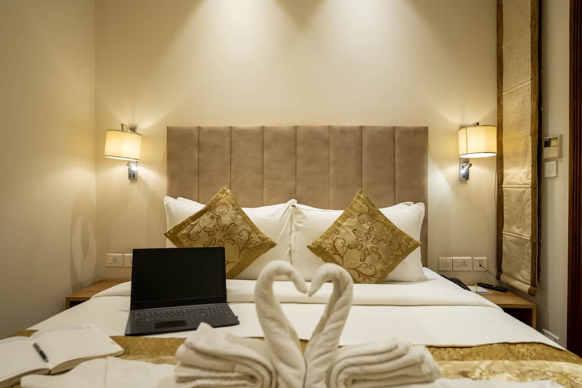 Una habitación de hotel con una cama, dos lámparas fijadas a la pared, una computadora portátil y una decoración de toallas con forma de corazón.