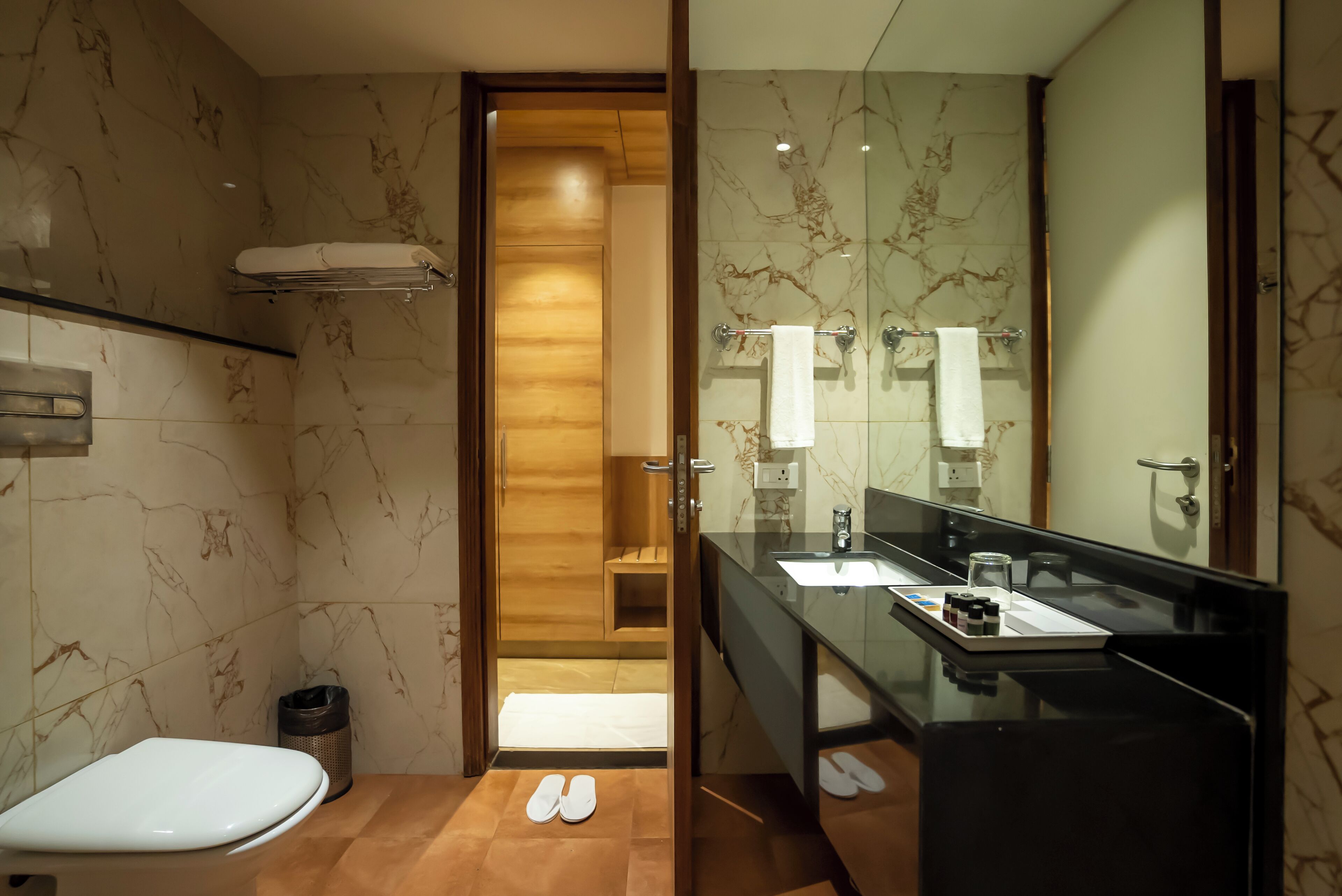 A modern bathroom with a marble floor, a white toilet, a glass shower enclosure, and a black sink with a mirror.