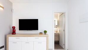 Un salon moderne avec un téléviseur à écran plat fixé à un meuble en bois, une cafetière rouge et une petite plante posée sur le meuble.