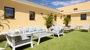 Une terrasse avec des meubles blancs, une petite table et une plante en pot.