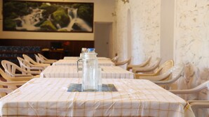 Un comedor con mesas dispuestas para una comida, una jarra de agua y un cuadro grande en la pared.