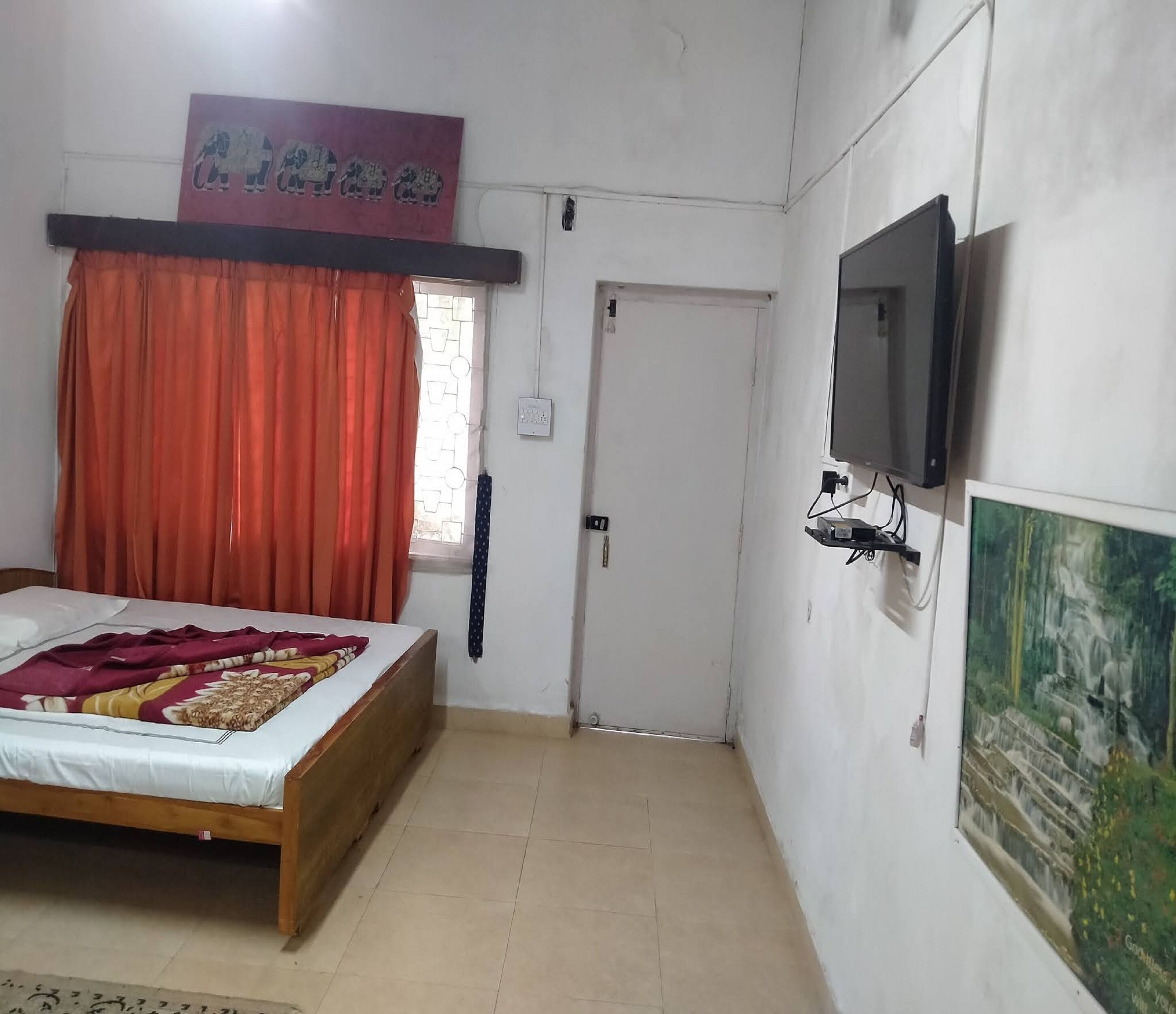 A bedroom with a bed, a television, a door, and a painting on the wall.