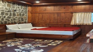 Una habitación de madera con cama, pared de piedra y ventana con cortinas.