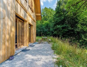 Una cabaña de madera con un camino de grava que lleva a una mesa de picnic rodeada de un bosque denso.