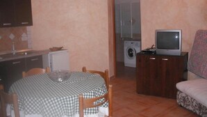 Un espacio habitable compacto con una mesa de comedor, sillas, un sofá, un televisor, una lavadora y una cocina con armarios y salpicadero de azulejos.