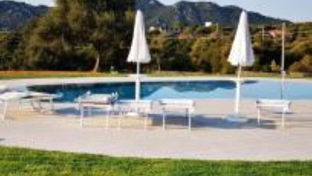 Una piscina con sillas de descanso y sombrillas, rodeada de césped y montañas al fondo.