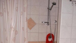 Zona de ducha con mampara de vidrio, dispensador de jabón rojo y cabezal de ducha.