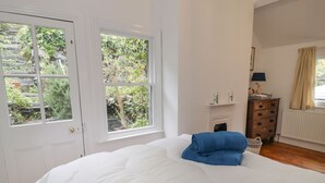 A bedroom with a large bed, white walls, a fireplace, and a view of greenery through the windows. - Wenallt (Porthmadog)