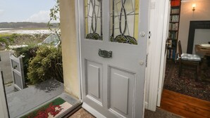 A door with stained glass, a view of the sea, and a room with a rug and bookshelves. - Wenallt (Porthmadog)