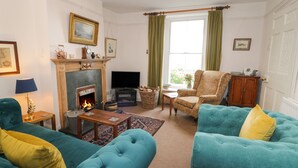 A living room with teal sofas, a fireplace, a television, and a window with curtains. - Wenallt (Porthmadog)