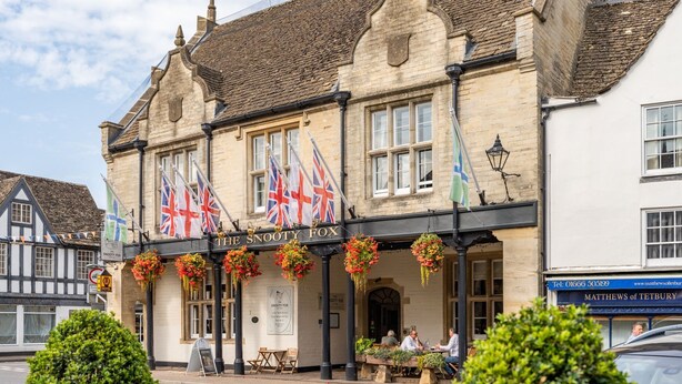 A traditional pub with multiple flags, outdoor seating, and a sign for 'The Sooty Fox'. - Christmas Cottage - in Tetbury (Tetbury)