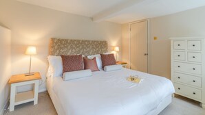 A neatly arranged bedroom with a large bed, two bedside tables, a dresser, and a door. - Christmas Cottage - in Tetbury (Tetbury)