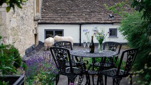 A round metal table with chairs in a garden setting, a bottle of wine, and a vase with flowers. - Christmas Cottage - in Tetbury (Tetbury)