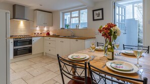 A modern kitchen with white cabinets, a built-in oven, and a dining area with a wooden table set for two. - Christmas Cottage - in Tetbury (Tetbury)
