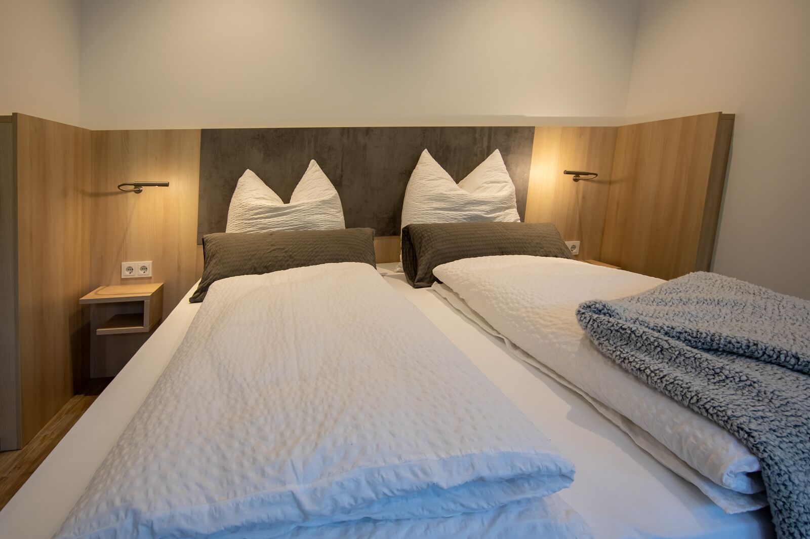 A double bed with a wooden headboard, two bedside tables, and a blanket on the right side.