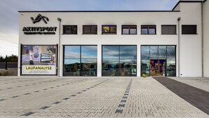 Um edifício moderno com amplas janelas de vidro e um letreiro para 'AktivSport', oferecendo serviço de câmeras de alta velocidade e análise de movimento.