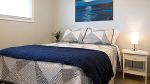 Une chambre à coucher avec un lit, une table de chevet, une lampe, un tableau et une fenêtre.