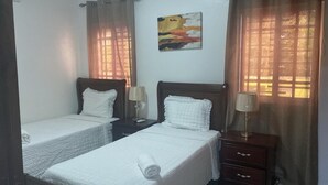 Una habitación de hotel con dos camas individuales, una mesita de noche con lámpara, una pequeña mesa y un cuadro colgado en la pared.