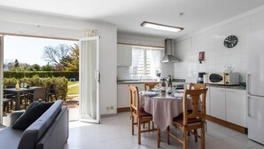 A modern kitchen with white cabinets, a dining table set for four, and a sofa in the adjacent living area. - 2 Bedroom Duplex Apartment in Puerto Pollensa (Puerto Pollensa)