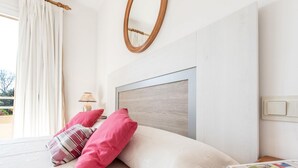 A bedroom with a bed, pillows, a nightstand, a lamp, a mirror, and a window with curtains. - 2 Bedroom Duplex Apartment in Puerto Pollensa (Puerto Pollensa)