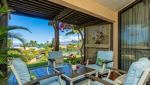 A covered outdoor seating area with a table, chairs, and a view of the landscape. - Townhouse Retreat with Ocean Views From Upper & Lower Lanai - Wailea Ekahi #30B (Wailea, Maui)