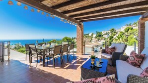 A covered patio with a table and chairs, a sofa, and a view of the sea and hills. - Villa Estrella with private heated pool and breathtaking views (AN)