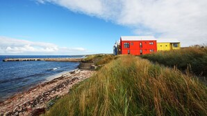 Een kustgezicht met een rood en geel gebouw, een steiger en een rotsachtige kustlijn.