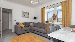 A modern living room with a grey sectional sofa, a white marble table, and a large window with curtains. - Dun Buidhe (South Uist)
