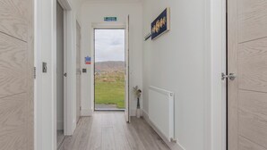 A hallway with a view of a grassy field and mountains through a glass door. - Dun Buidhe (South Uist)