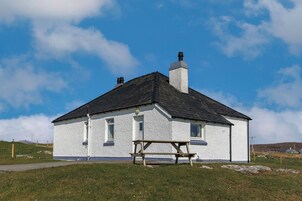 Un pequeño edificio blanco con techo negro, una chimenea y una mesa de picnic al frente.